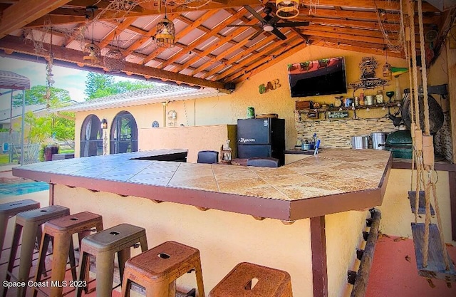 exterior space featuring vaulted ceiling, a kitchen breakfast bar, and black fridge