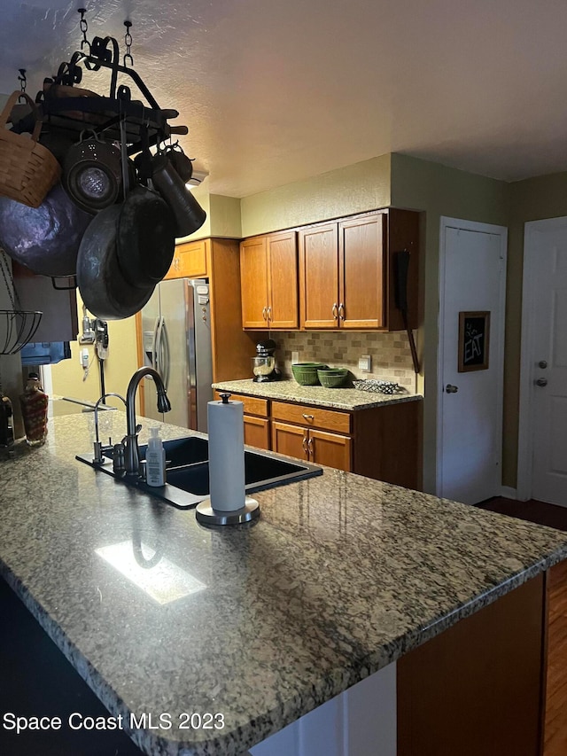 kitchen featuring sink, dark stone counters, stainless steel fridge with ice dispenser, backsplash, and an inviting chandelier