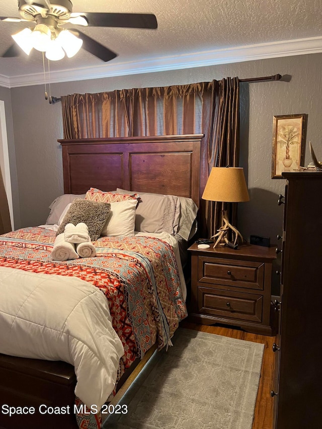 bedroom featuring ceiling fan, a textured ceiling, crown molding, and dark wood-type flooring