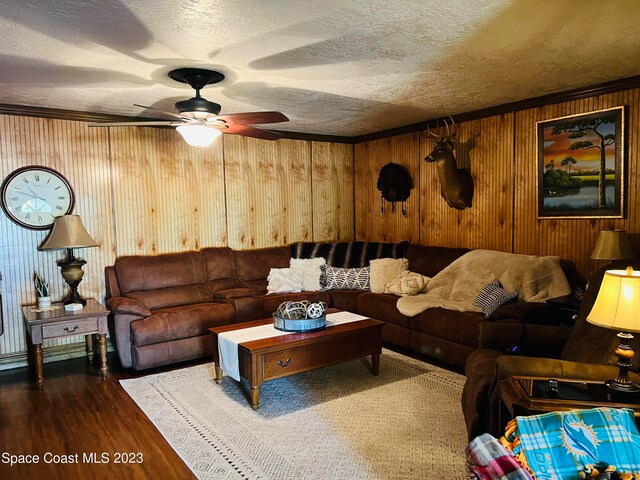 living room featuring dark hardwood / wood-style floors, wood walls, a textured ceiling, and ceiling fan