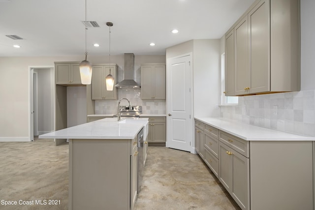 kitchen featuring wall chimney exhaust hood, an island with sink, decorative light fixtures, and tasteful backsplash