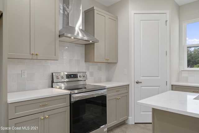 kitchen with gray cabinets, stainless steel range with electric stovetop, backsplash, light stone countertops, and wall chimney range hood