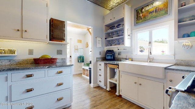 kitchen with sink, white cabinets, light hardwood / wood-style floors, range, and light stone countertops