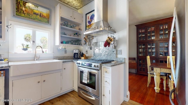 kitchen with sink, stainless steel stove, wall chimney exhaust hood, white cabinetry, and light wood-type flooring