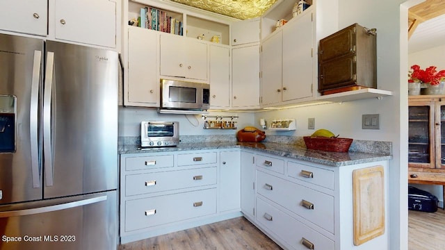 kitchen featuring white cabinets, stainless steel appliances, stone countertops, and light wood-type flooring