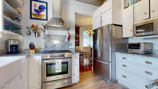 kitchen featuring white cabinetry, light hardwood / wood-style floors, stainless steel appliances, a chandelier, and wall chimney range hood