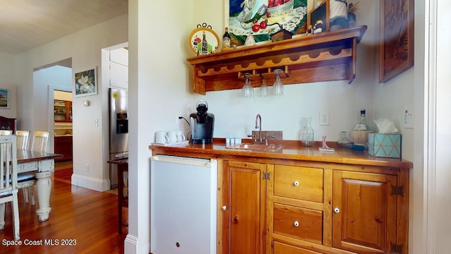 bar featuring refrigerator, stainless steel fridge with ice dispenser, dark wood-type flooring, and sink