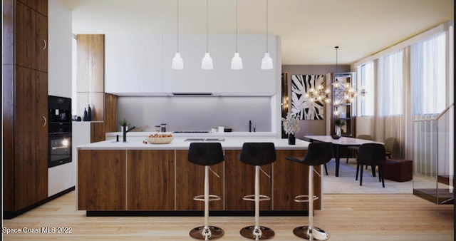 kitchen featuring decorative light fixtures, a kitchen breakfast bar, an island with sink, light wood-type flooring, and white cabinets