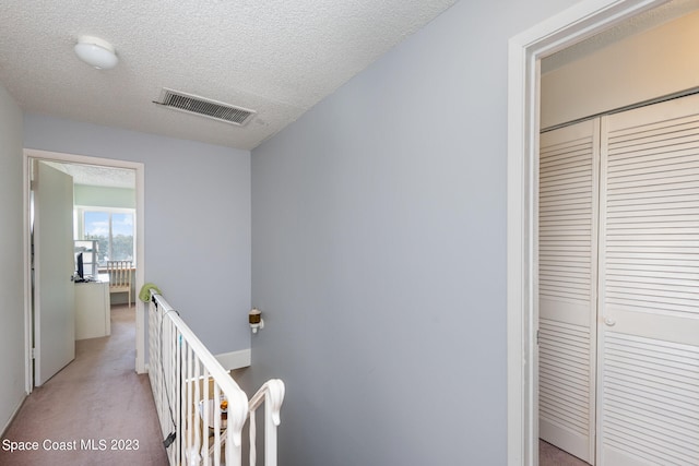 hallway with a textured ceiling and light colored carpet