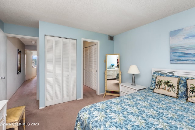 bedroom featuring a textured ceiling, multiple closets, and light colored carpet