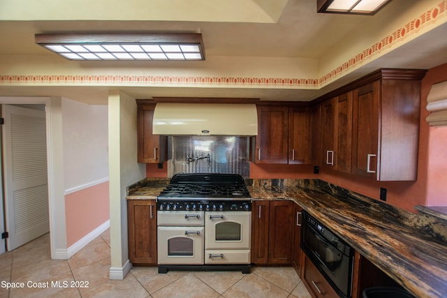 kitchen with dark stone countertops, double oven range, light tile floors, and wall chimney range hood