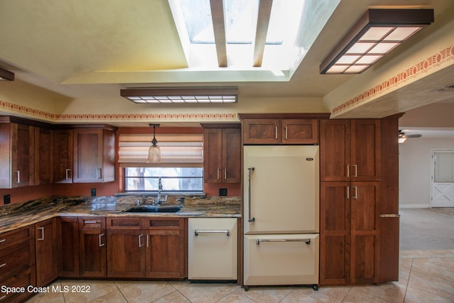 kitchen with pendant lighting, a skylight, white appliances, dark stone countertops, and sink