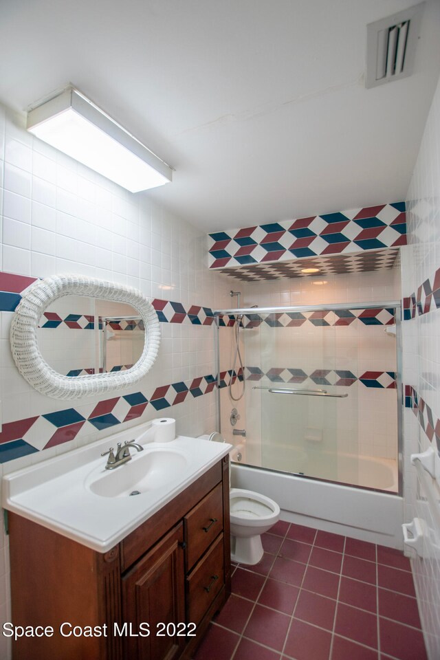 full bathroom featuring tile walls, toilet, bath / shower combo with glass door, tile flooring, and vanity