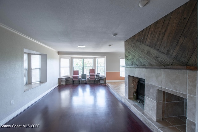 unfurnished living room with a tile fireplace, ornamental molding, dark wood-type flooring, and a textured ceiling