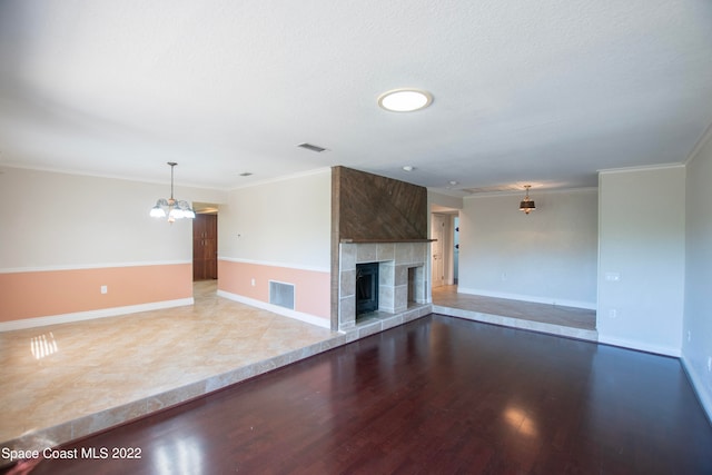 unfurnished living room featuring crown molding, an inviting chandelier, wood-type flooring, and a fireplace