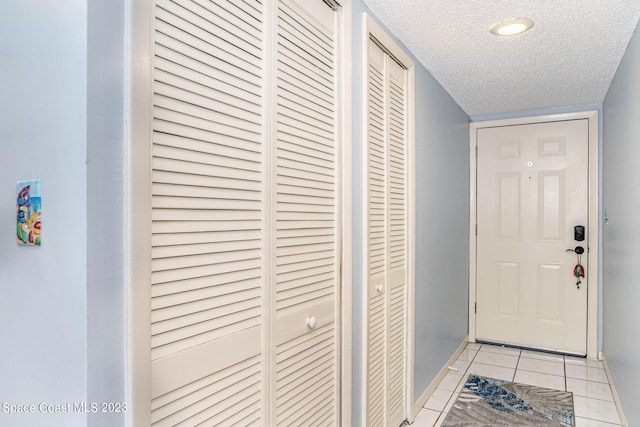 doorway with a textured ceiling and light tile patterned floors