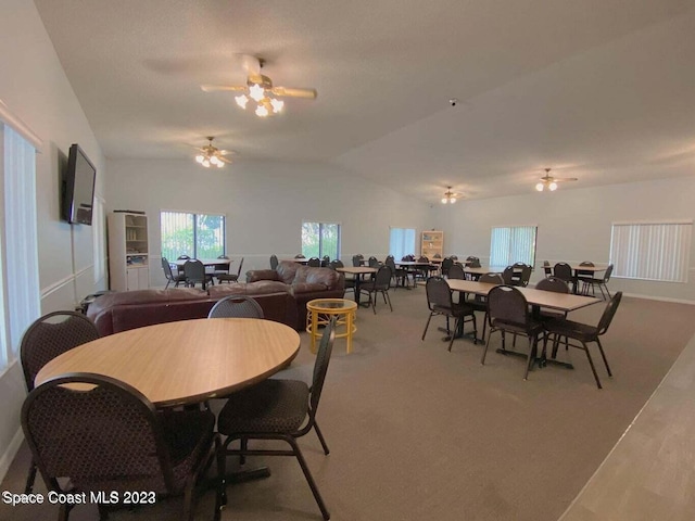 carpeted dining space with ceiling fan and vaulted ceiling