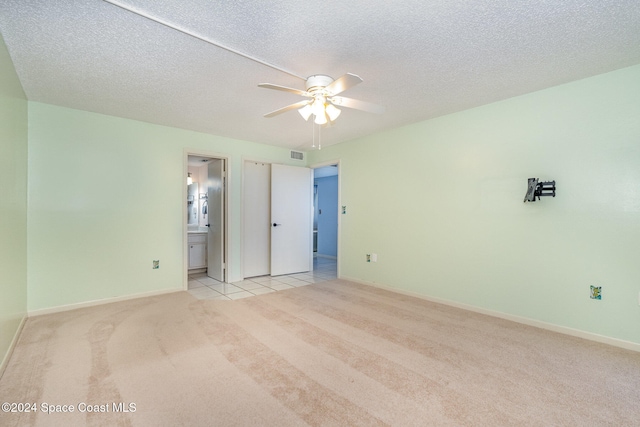 unfurnished bedroom featuring ensuite bathroom, ceiling fan, a textured ceiling, and light colored carpet