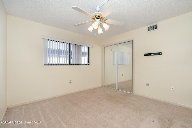 unfurnished bedroom featuring ceiling fan, a textured ceiling, a closet, and light colored carpet