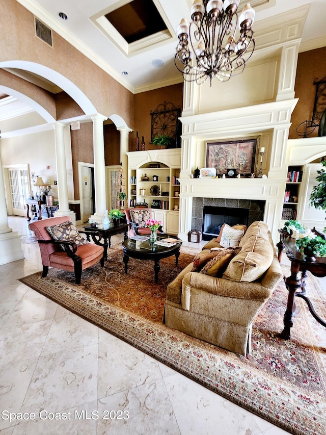 living room featuring a chandelier, light tile floors, ornamental molding, a tiled fireplace, and decorative columns