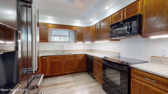 kitchen with ceiling fan, black appliances, a tray ceiling, light wood-type flooring, and sink