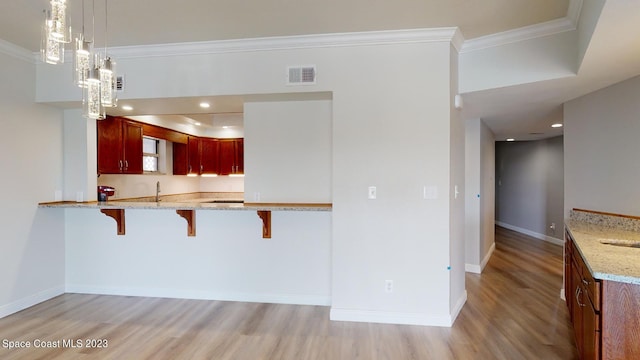 kitchen with sink, light stone counters, a kitchen breakfast bar, hanging light fixtures, and light wood-type flooring