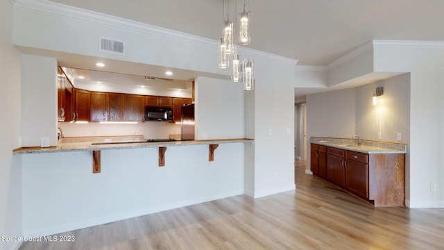 kitchen featuring light stone countertops, decorative light fixtures, light hardwood / wood-style floors, crown molding, and stainless steel refrigerator