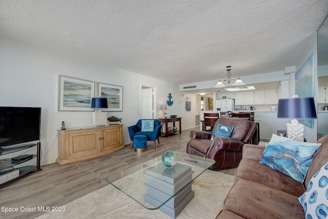 living room featuring a notable chandelier, a textured ceiling, and light hardwood / wood-style flooring