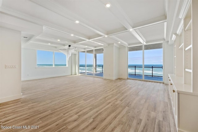 empty room featuring coffered ceiling, a water view, floor to ceiling windows, and light hardwood / wood-style flooring