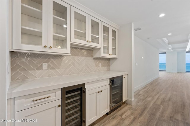 bar featuring backsplash, wine cooler, light wood-type flooring, and white cabinetry