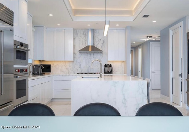 kitchen with appliances with stainless steel finishes, backsplash, light tile flooring, and wall chimney range hood