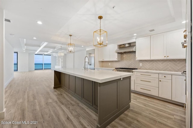 kitchen featuring backsplash, a kitchen island with sink, light wood-type flooring, white cabinets, and wall chimney exhaust hood