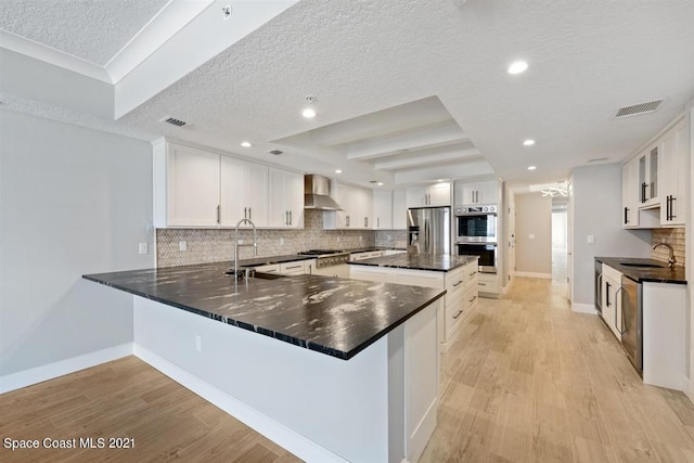 kitchen with wall chimney range hood, white cabinetry, backsplash, and stainless steel appliances