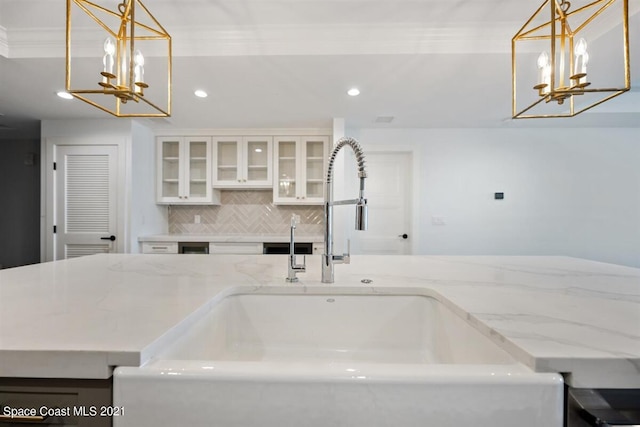 kitchen featuring crown molding, decorative light fixtures, sink, and light stone countertops