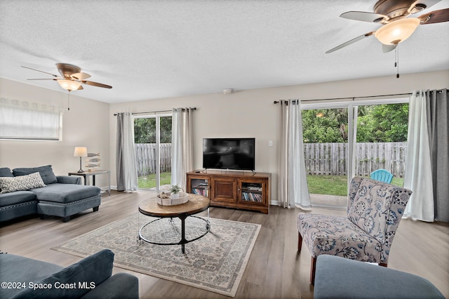 living room with light hardwood / wood-style floors, a textured ceiling, and ceiling fan