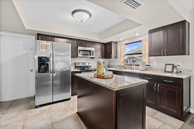 kitchen featuring a kitchen island, dark brown cabinets, stainless steel appliances, and a tray ceiling