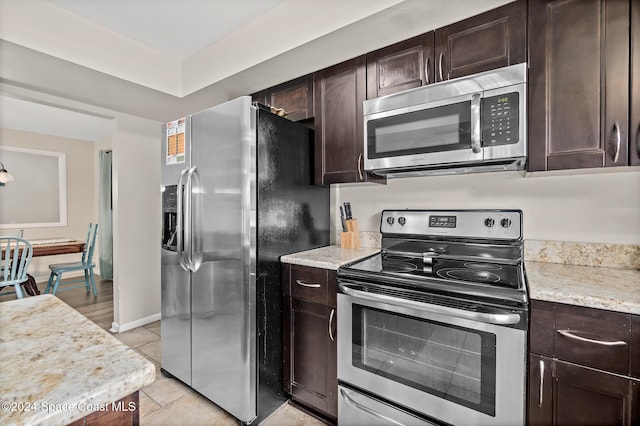 kitchen featuring dark brown cabinetry, stainless steel appliances, light stone counters, and light tile patterned floors