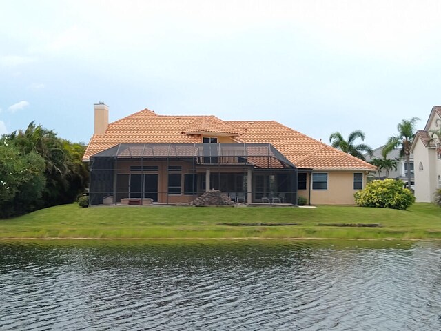 rear view of house featuring a yard, a water view, a balcony, and glass enclosure