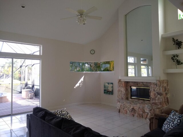 living room featuring light tile patterned flooring, a high ceiling, a stone fireplace, and ceiling fan