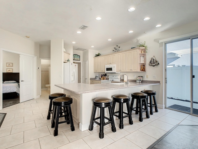 kitchen featuring white appliances, kitchen peninsula, light tile patterned floors, and a kitchen bar