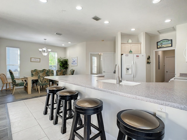 kitchen featuring a breakfast bar area, a chandelier, pendant lighting, sink, and white refrigerator with ice dispenser