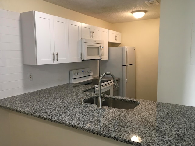 kitchen with white appliances, sink, dark stone countertops, white cabinets, and a textured ceiling