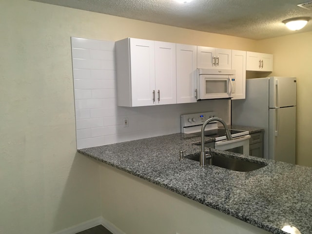 kitchen with white appliances, a textured ceiling, white cabinetry, and dark stone counters