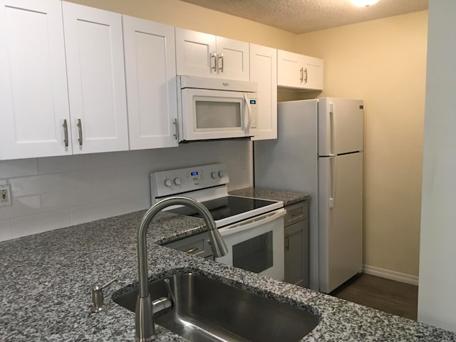 kitchen with white appliances, dark stone countertops, dark wood-type flooring, a textured ceiling, and white cabinetry