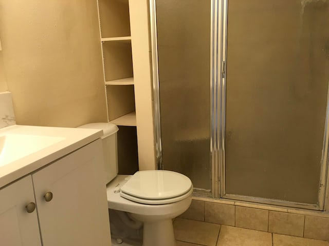 bathroom with tile floors, toilet, vanity, and a shower with door