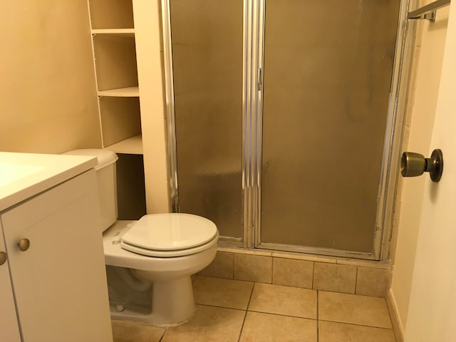 bathroom featuring toilet, vanity, a shower with shower door, and tile flooring