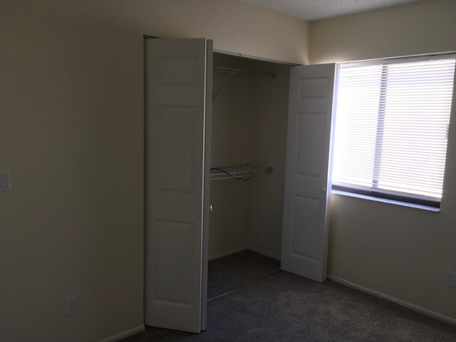 unfurnished bedroom with dark carpet and a closet