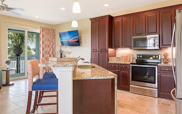 kitchen with pendant lighting, ceiling fan, light stone counters, a kitchen breakfast bar, and appliances with stainless steel finishes