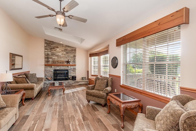 living room with a stone fireplace, vaulted ceiling, ceiling fan, and light wood-type flooring