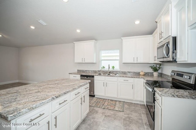 kitchen featuring stainless steel appliances, white cabinetry, sink, light stone countertops, and a kitchen island